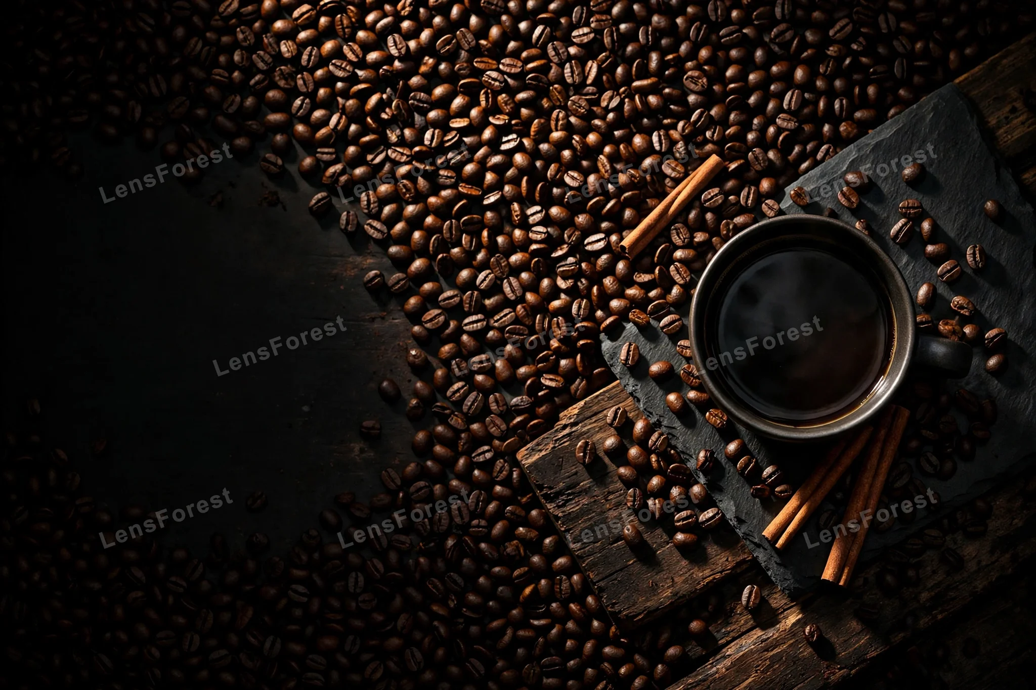 Moody overhead flat lay of dark roasted coffee beans with a cup of black coffee and cinnamon sticks on dark slate with copy space on one side