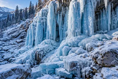 A winter waterfall frozen in ice with long icicles, snow banks and a partially flowing stream below
